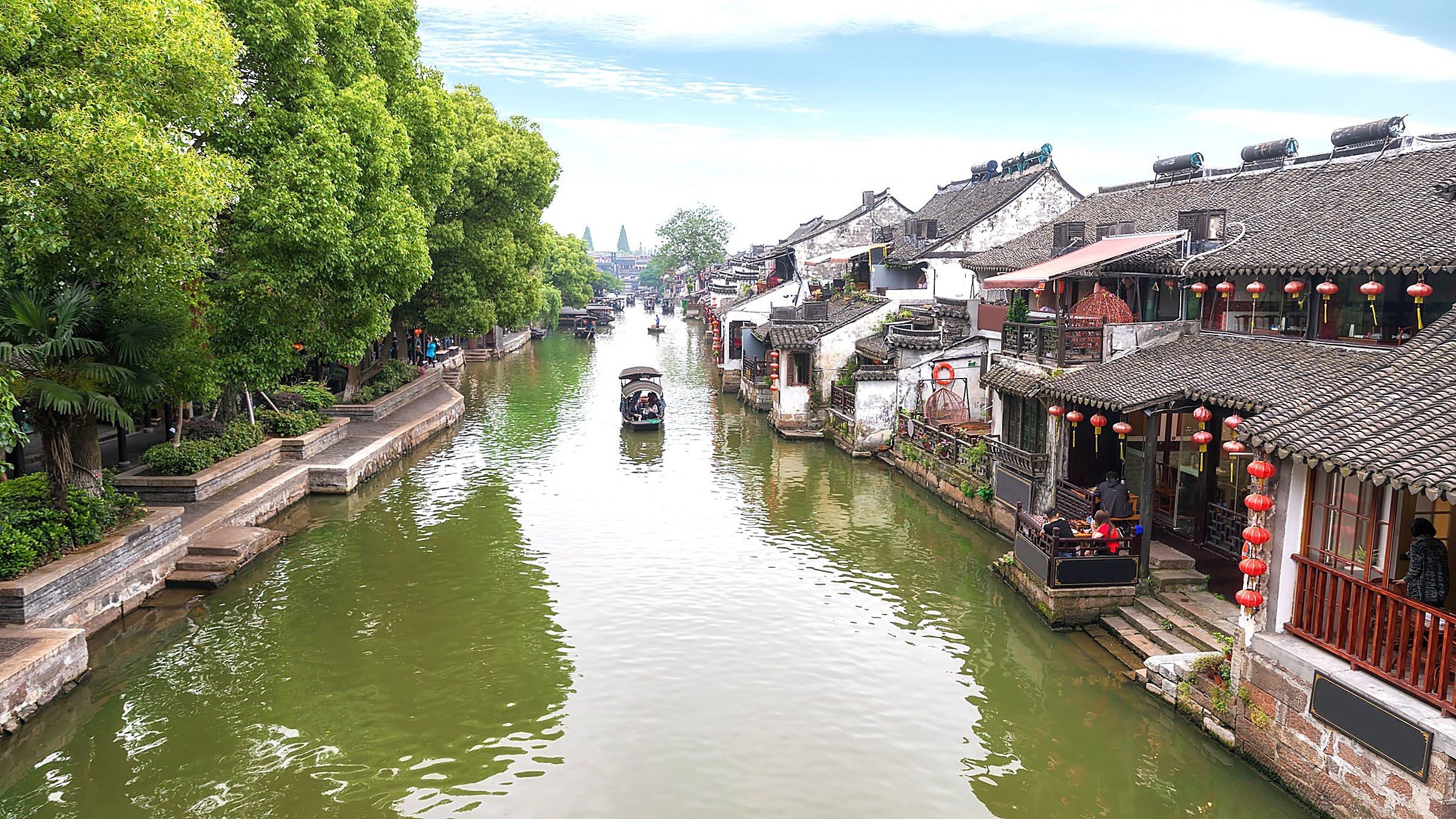 Pingjiang Road — a 1,600-year-old canal with stone bridges, whitewashed Suzhou-style houses, and willow trees, with small boats passing under the bridges