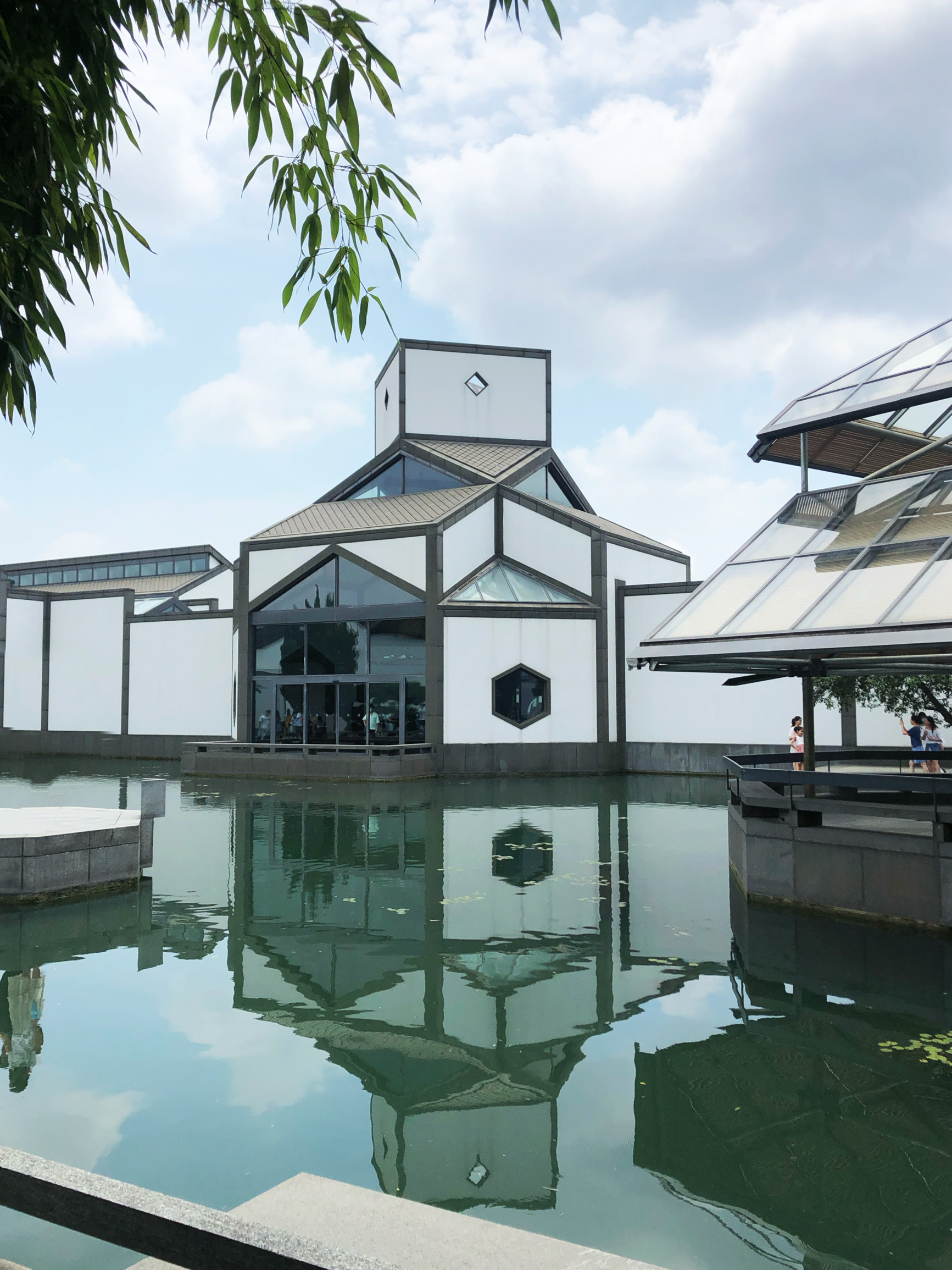 Suzhou Museum — I.M. Pei's 2006 modernist masterpiece with white walls and dark tile roofs, reflected in a rectangular pool in the central courtyard, with a rock garden in the background