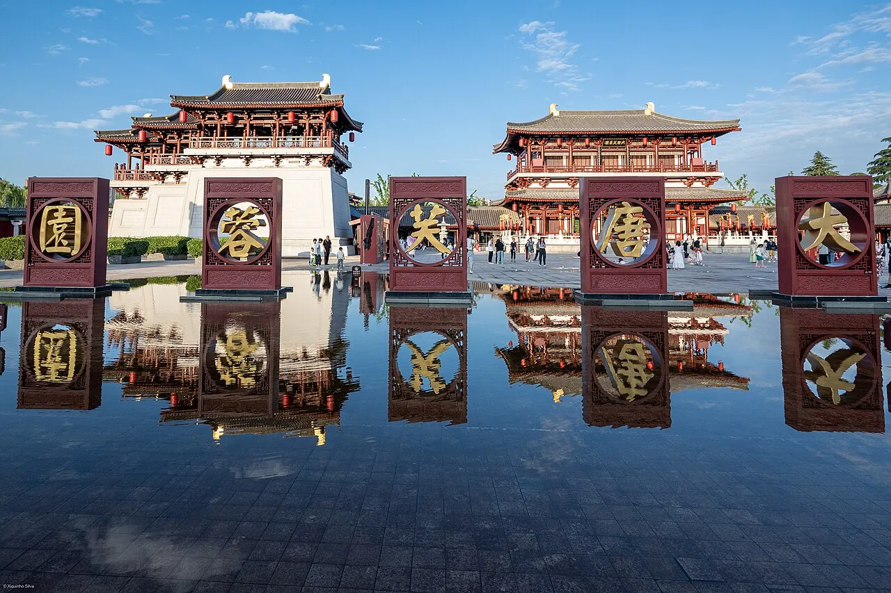 Tang Paradise (Datang Furong Yuan) in Xi'an, with six golden calligraphy panels spelling 'Great Tang Hibiscus Garden' reflected in a still pool under a clear blue sky.