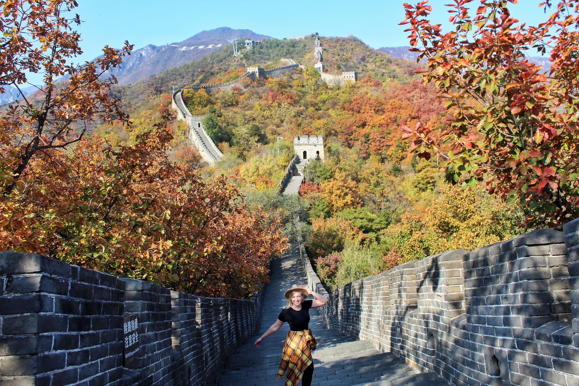The Great Wall of China at Mutianyu in autumn, with restored Ming-era watchtowers and crenellated battlements snaking along forested mountain ridges under soft afternoon light, Beijing municipality
