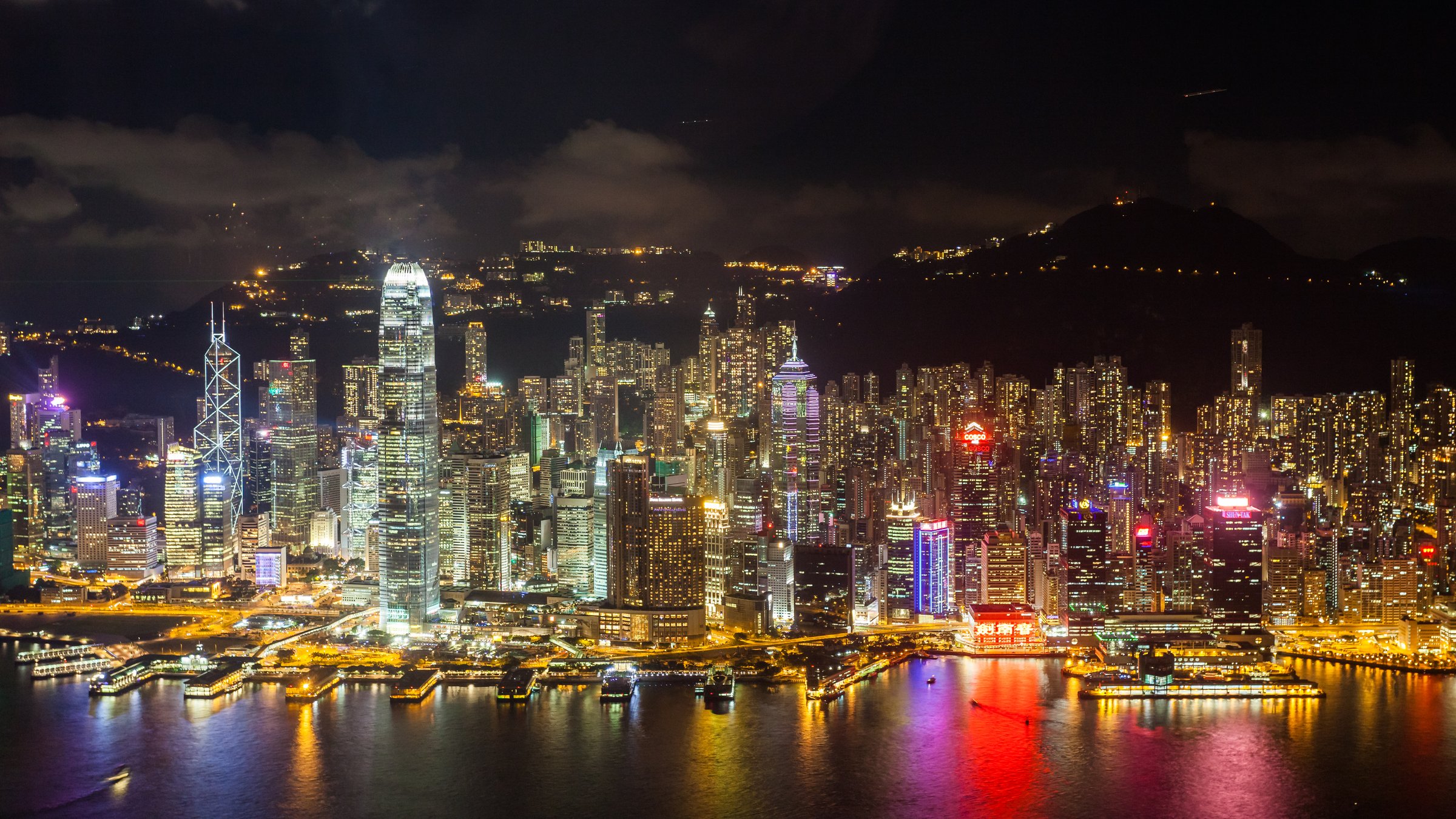 Hong Kong Puerto Victoria de noche con el icónico horizonte de rascacielos reflejándose en el agua y el paseo marítimo de Kowloon en primer plano