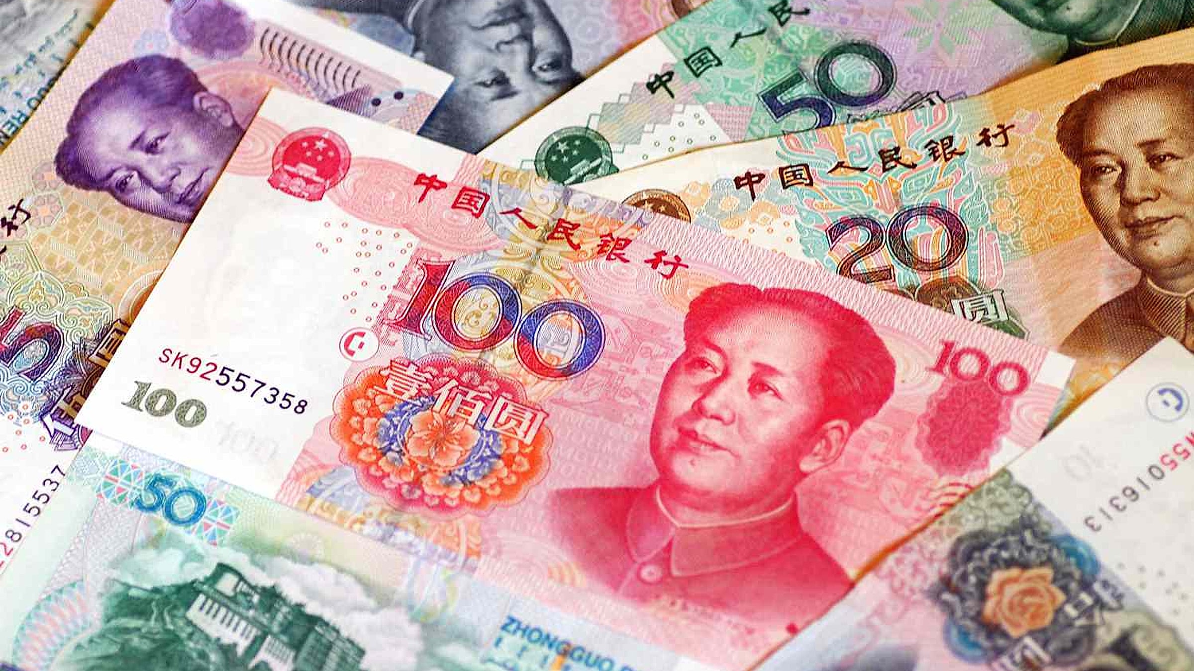 Nahaufnahme ausgebreiteter bunter chinesischer RMB-Banknoten – vergleichen Sie damit den Metallstreifen, die farblich wechselnden Ziffern und den erhabenen Aufdruck auf dem Kragen, die echte von gefälschten Banknoten unterscheiden