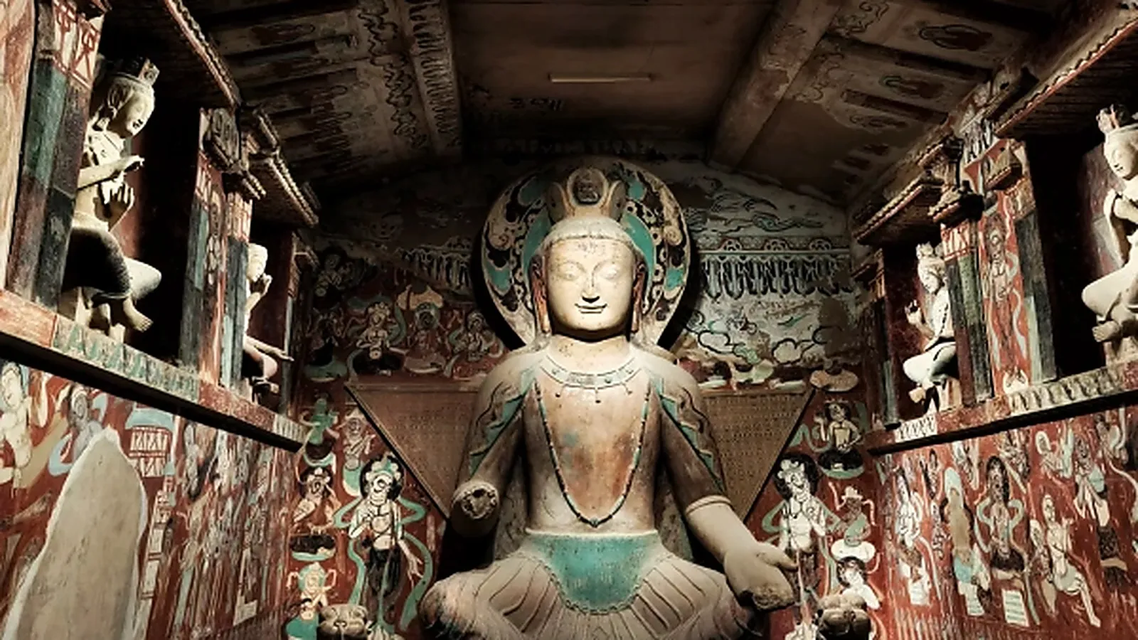 Buddha Maitreya duduk dari Gua 275 di Dunhuang — patung Dinasti Wei Utara setinggi 3,4 m dari tahun 460 M, salah satu patung Buddha tertua di kompleks Mogao, dengan pigmen merah muda dan hijau asli masih terlihat pada jubah dan pose silang-pergelangan kaki yang khas dari pahatan gua Buddha awal di sepanjang Jalur Sutra — satu-satunya tempat di mana detail level ini bisa dilihat adalah di replika Museum Dunhuang atau di gua ini dengan tiket tur berpemandu khusus