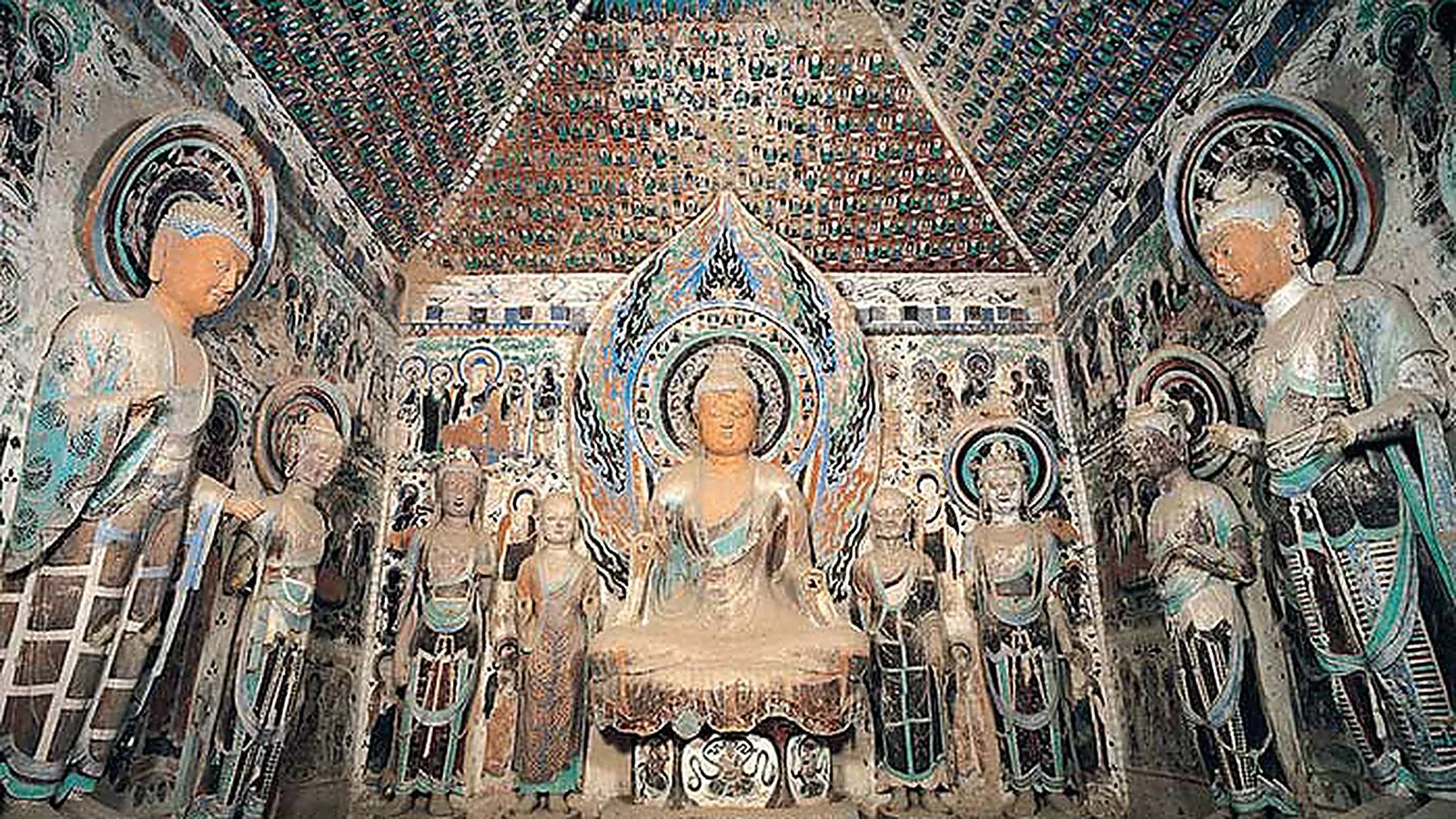 Interior Gua Mogao di Dunhuang — patung Buddha duduk pusat diapit oleh bodhisattva pengiring dan deretan figur yang lebih kecil, dinding dan langit-langit ditutupi fresko Dinasti Tang berusia 1.600 tahun berupa Buddha-Buddha kecil dalam pigmen hijau, merah, dan oker, warna cat asli masih terlihat di tempat mural dilindungi dari cahaya dan sentuhan — Gua 220 adalah salah satu gua yang paling banyak dikunjungi dan contoh khas gua-gua bergaya era Tang tinggi yang menjadi terkenal dari kompleks Mogao