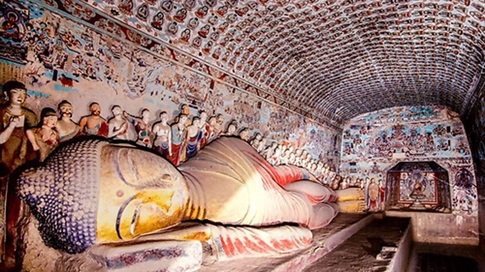 Buddha berbaring 15 m (涅槃像) dari Gua 148 di Gua Mogao — patung Dinasti Tang berusia 1.500 tahun yang menunjukkan Buddha memasuki nirwana, dengan kepala menghadap ke pengunjung dan lengan kanan menopang kepala, dikelilingi oleh deretan patung murid dengan jubah bergambar di dinding belakang — salah satu patung Buddha indoor terbesar di kompleks Mogao dan patung tunggal yang paling banyak difoto di gua-gua yang dapat diakses