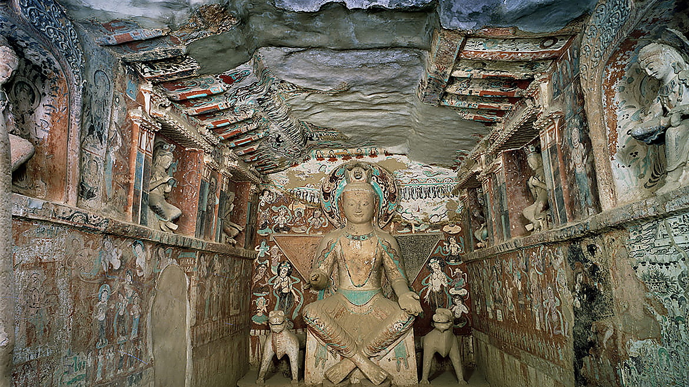 Interior of Mogao Cave 9 in Dunhuang, Gansu, with late-Tang Buddhist murals covering the walls and ceiling, featuring the central Buddha figure surrounded by painted bodhisattvas and donor figures in earth-tone pigments