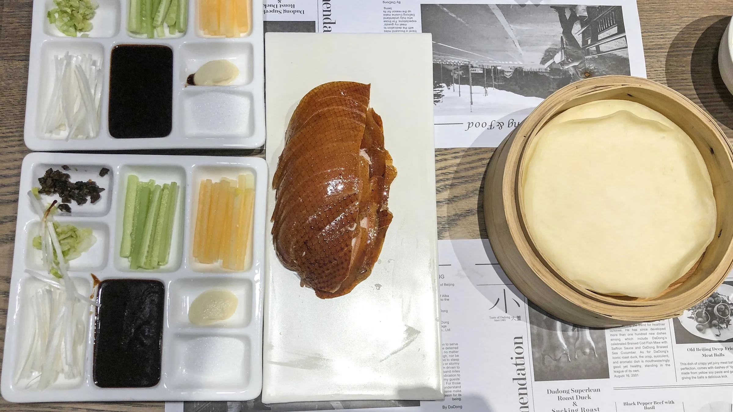 北京ダックガイド — ホーシン醤、ねぎ、薄餅と一緒に白い皿に盛られたカリカリの皮付きの丸ごとローストダック
