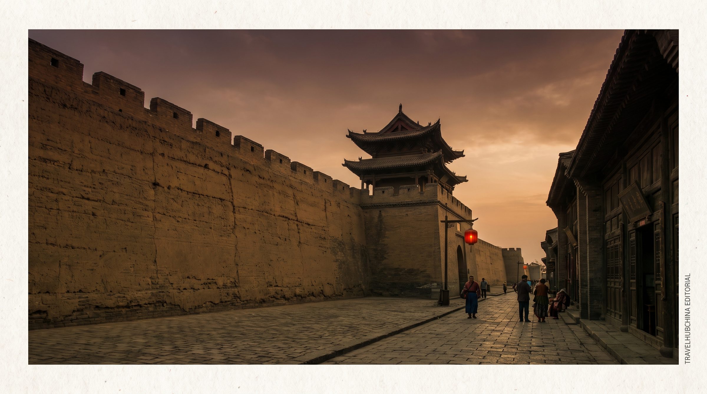 The Pingyao City Wall at sunset, with the East Tower silhouetted against an orange sky, lanterns along the wall top, and the rooftops of the ancient city visible below