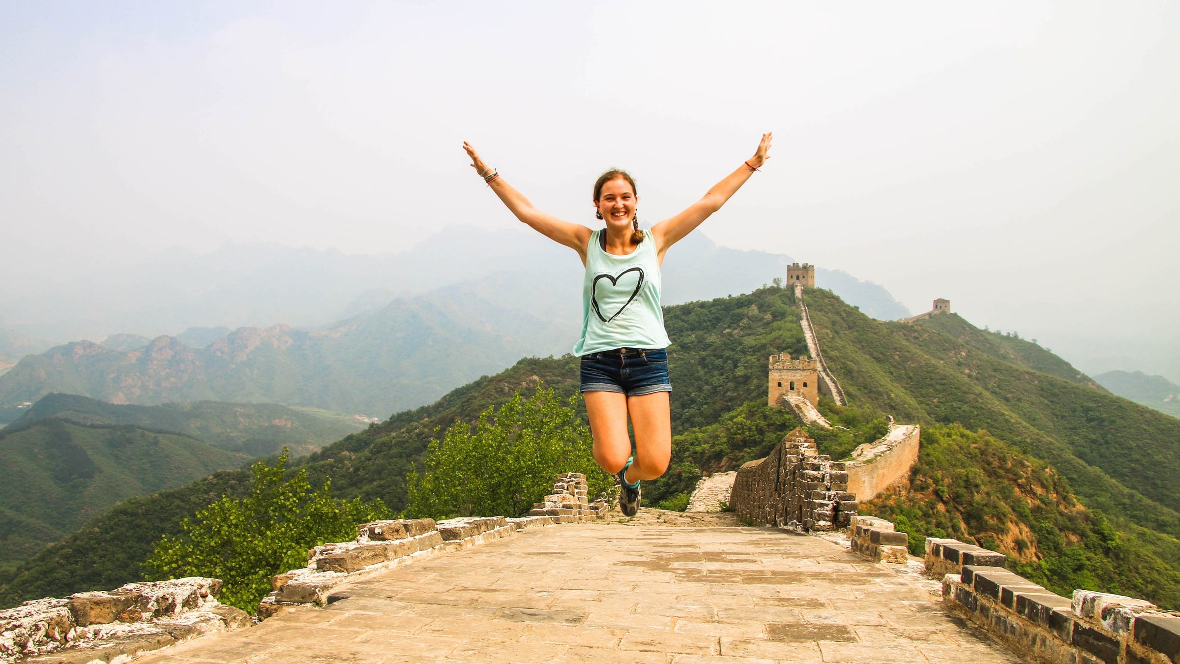 Solo female traveler joyfully jumping with arms raised on the Great Wall of China