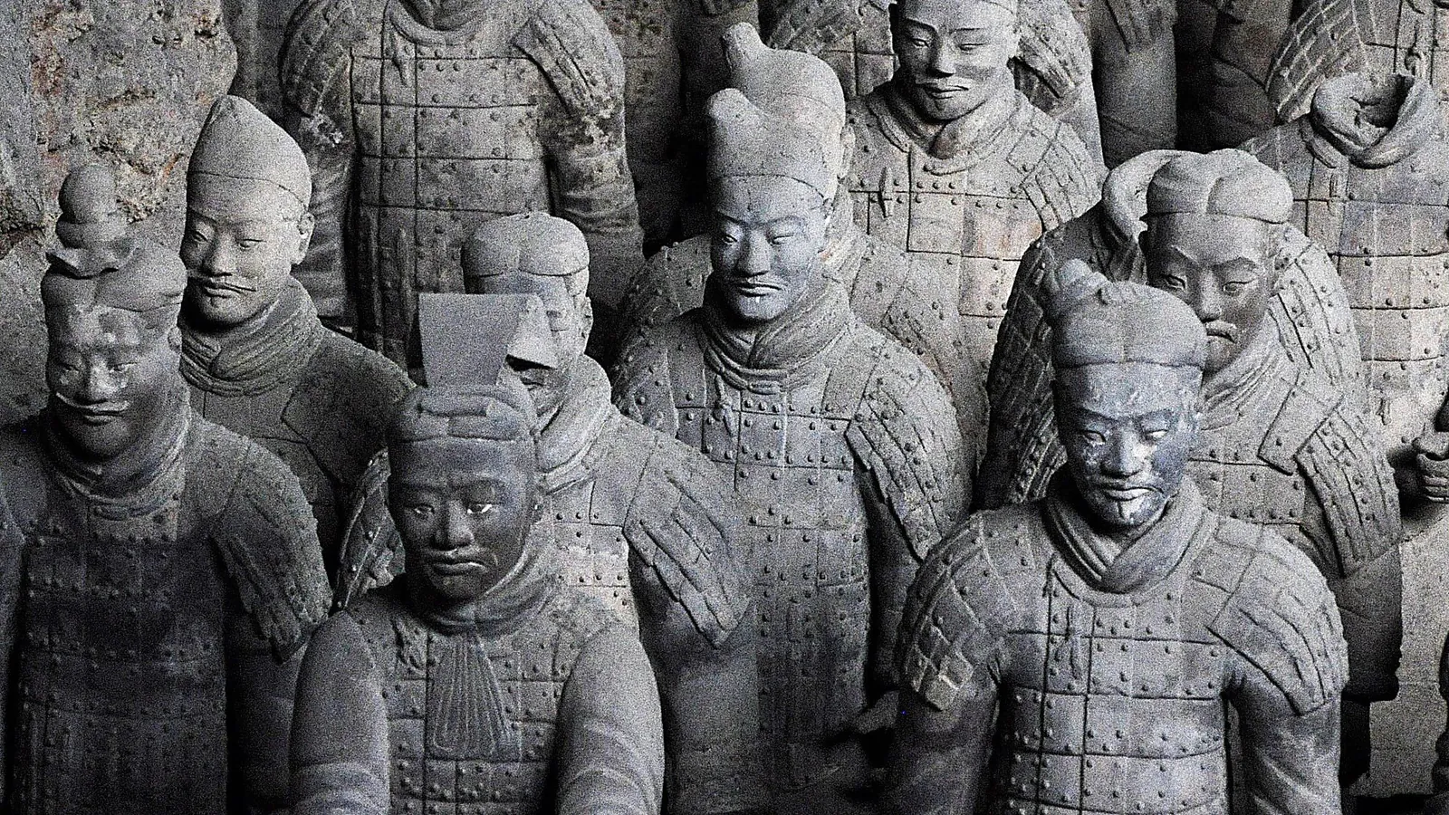 Close-up of Terracotta Army warriors in Pit 3 — the 2,200-year-old clay figures showing the individually sculpted faces, topknots, and detailed scale armor, with traces of the original purple and pink pigment visible on the cheeks and lips, the level of individuality that archaeologists say makes each warrior a unique portrait — Pit 3 has only 68 figures but they are the highest-ranking officers with the most elaborate armor of any pit