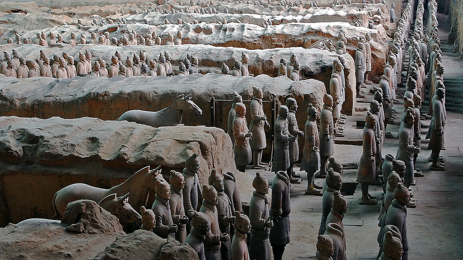 Pit 2 of the Terracotta Army at Xi'an — the kneeling archer and standing infantry in a partially excavated trench, with a real terracotta horse visible to the left, the 2,200-year-old clay figures still showing traces of their original pigment in good light, lined up in formation as the Qin-era craftsmen left them in 210 BC — the most-photographed trench in the museum because the eye-level view shows the detail on each warrior's face and armor