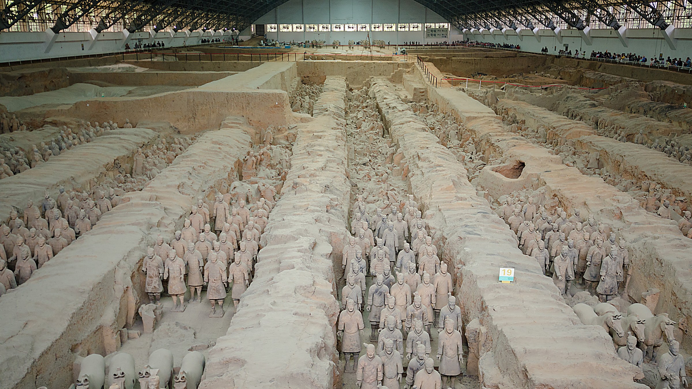 Rows of life-sized terracotta warriors standing in formation inside Pit 1 at the Terracotta Army museum near Xi'an, Shaanxi province, with excavation trenches and vaulted hangar roof overhead