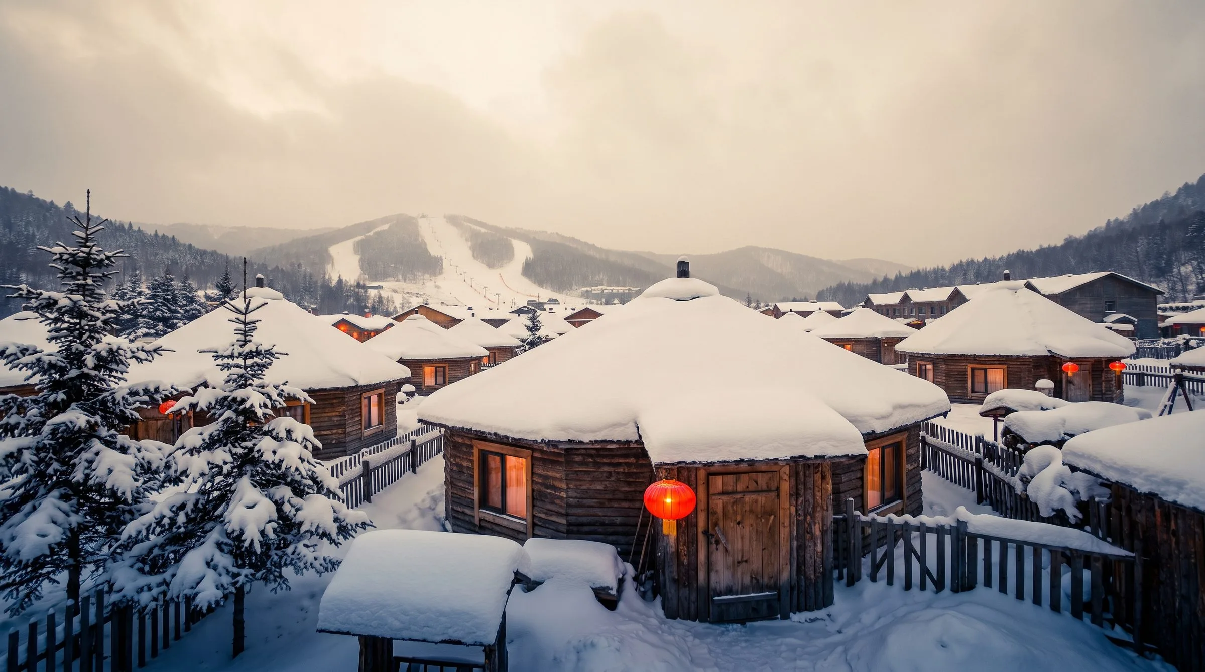 China Snow Town at night with red lanterns glowing against snow-covered wooden houses, snow piled high on rooftops under a deep blue winter sky